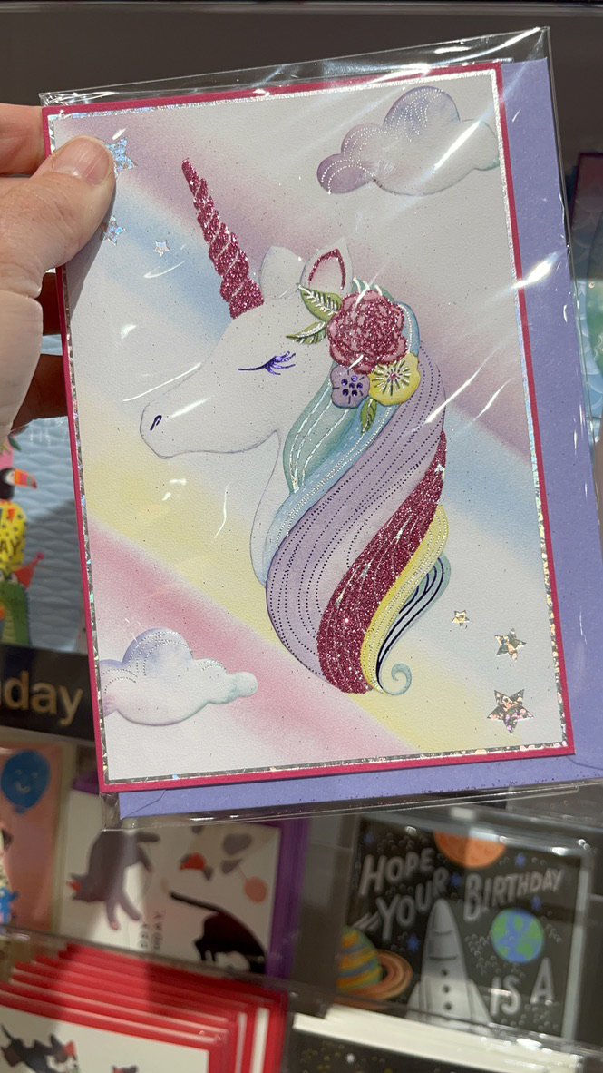 Licensed greeting card with unicorn design held in a retail store